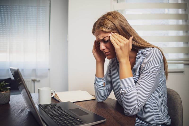 A stressed blonde woman rubbing her temples, sitting at her desk in front of a computer